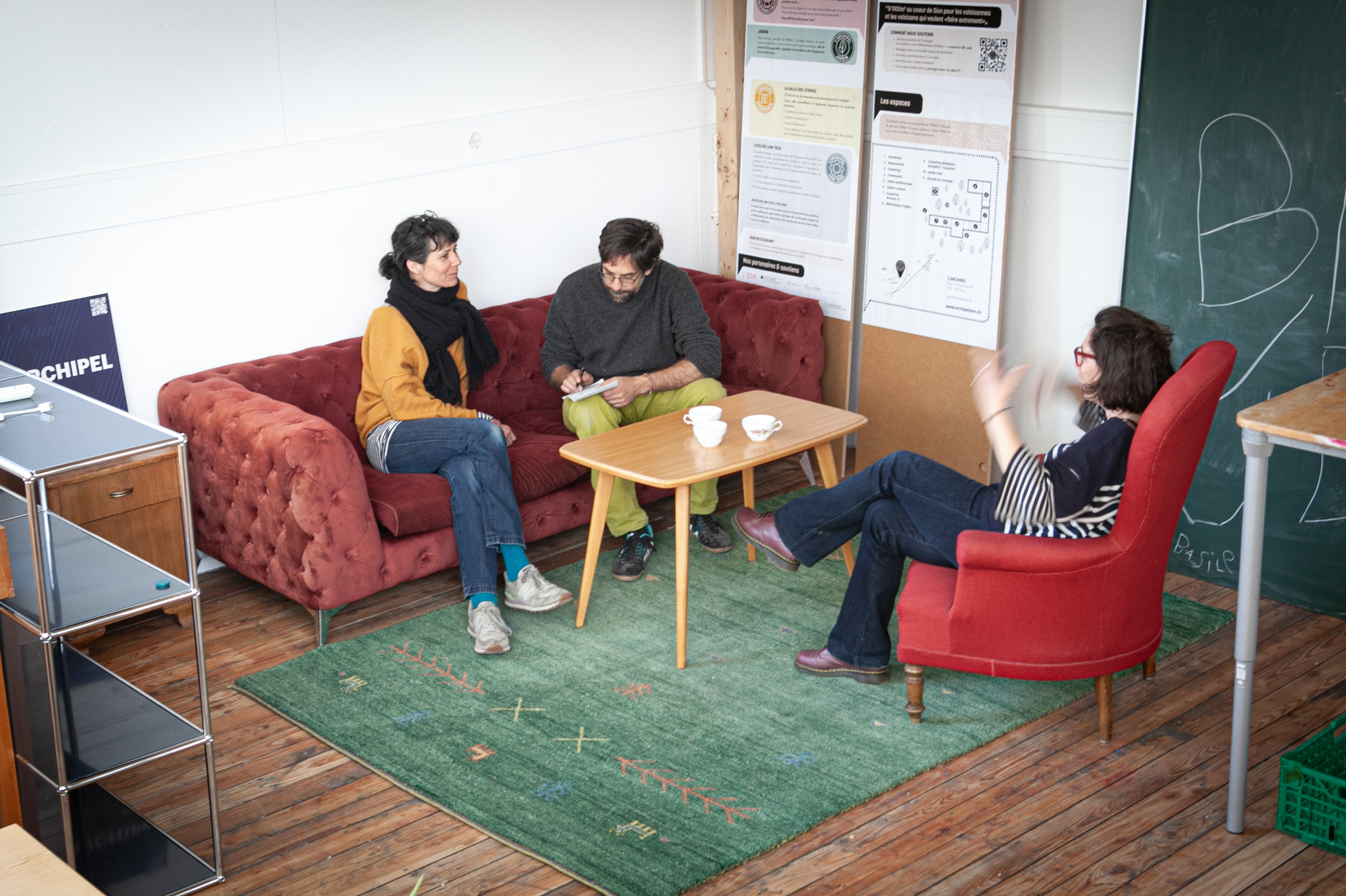 Image montrant notre coworking. On y voit trois personnes en train de discuter sur des canapés. Une table basse se trouve au milieu avec des tasses dessus.